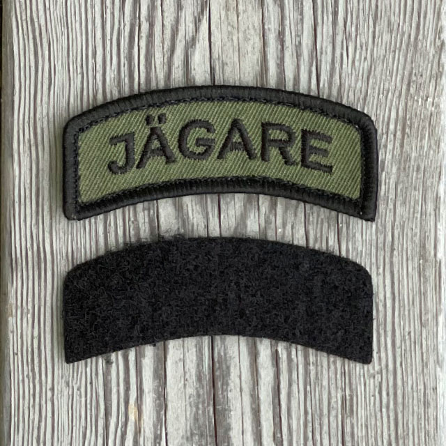JÄGARE Hook Patch Black/Green from TAC-UP GEAR with wood floor background and it´s separate black loop tab piece