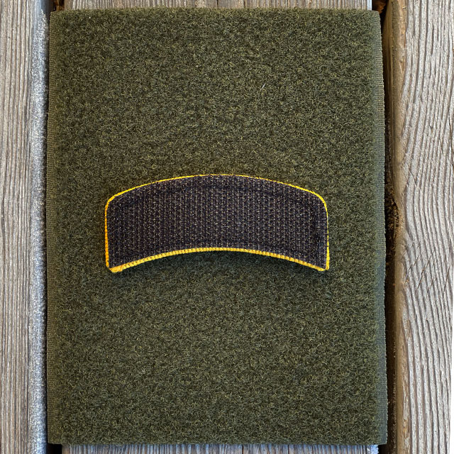 A JÄGARE Hook Patch Orange/Black face down on a pice of green loop fabric showing the hook backing in black