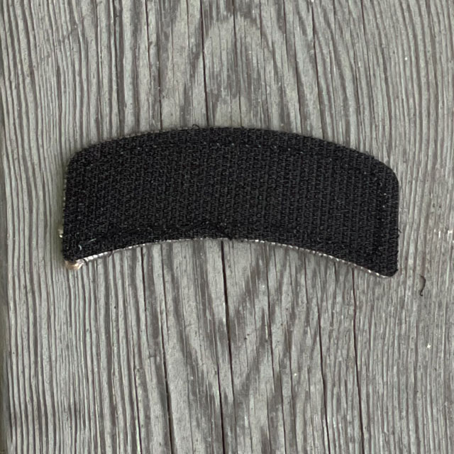 The back of a JÄGARE Hook Patch Silver Grey/White from TAC-UP GEAR with wooded floor background