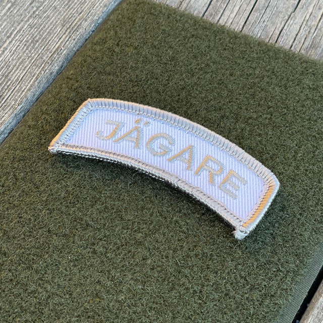 A JÄGARE Hook Patch Silver Grey/White from TAC-UP GEAR on green loop fabric seen from an angle