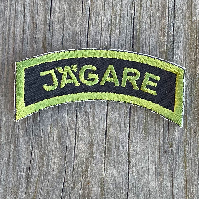A JÄGARE Patch Jungle Green on a wooded background.