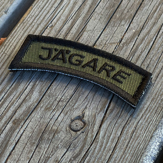 A JÄGARE K3 Type Hook Patch Black/Green seen from an angle lying on wooded floor