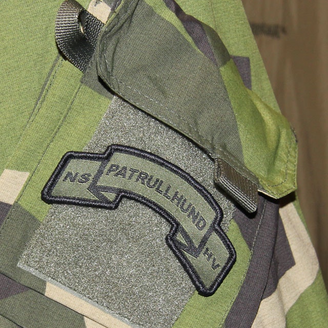 A mounted Patrullhund Hook Scroll Patch on a M90 camouflage NCWR Jacket.