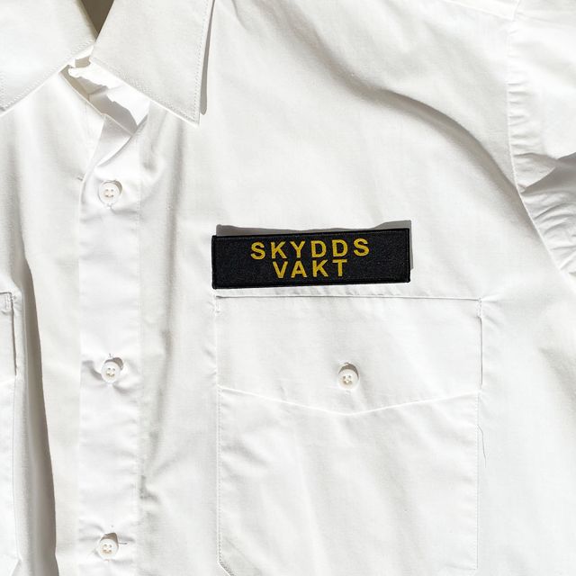 Skyddsvakt Avlångt Tygmärke på en vit skjorta direkt över vänster bröstficka