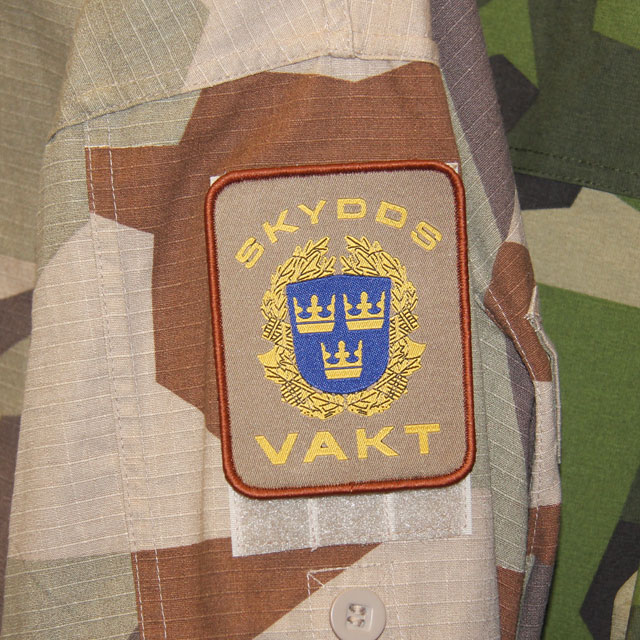Ett Skyddsvakt Tygmärke Kardborre Öken monterad på M90K jacka.
