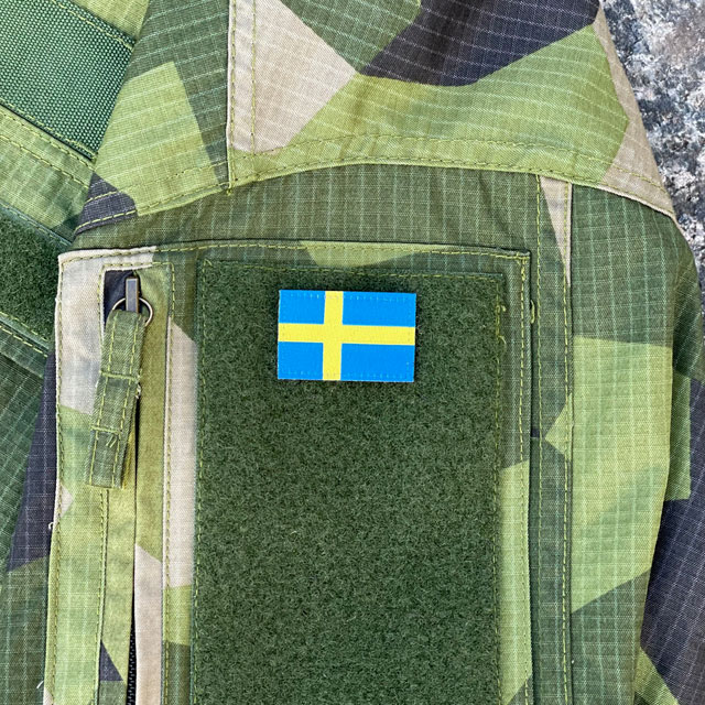 A Sweden Flag Hook Patch Arm seen mounted on a Fieldshirt in M90 camouflage
