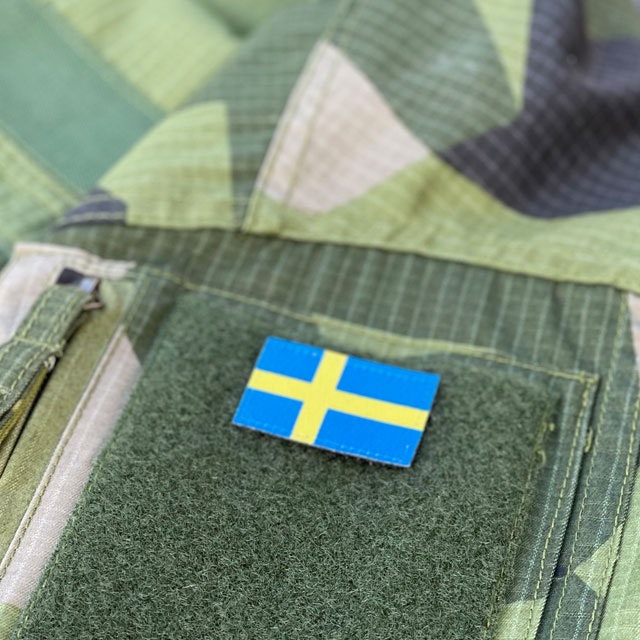 Seen from an angle and mounted on loop fabric is a Sweden Flag Hook Patch Arm