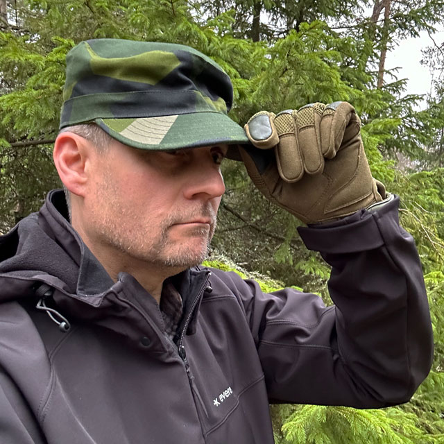 Touching the peak of a Patrol Cap M90 from TAC-UP GEAR on a model in the Swedish forest seen at a slight angle