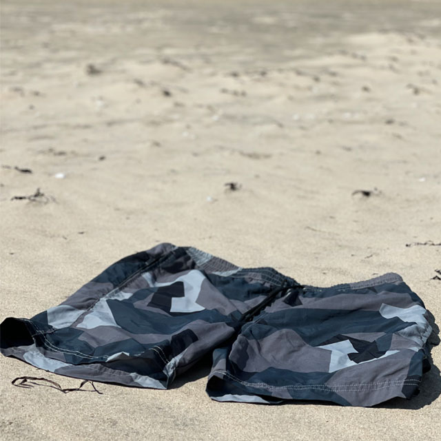 A pair of POSEIDON Swim Shorts M90 Grey from TAC-UP GEAR on a beach