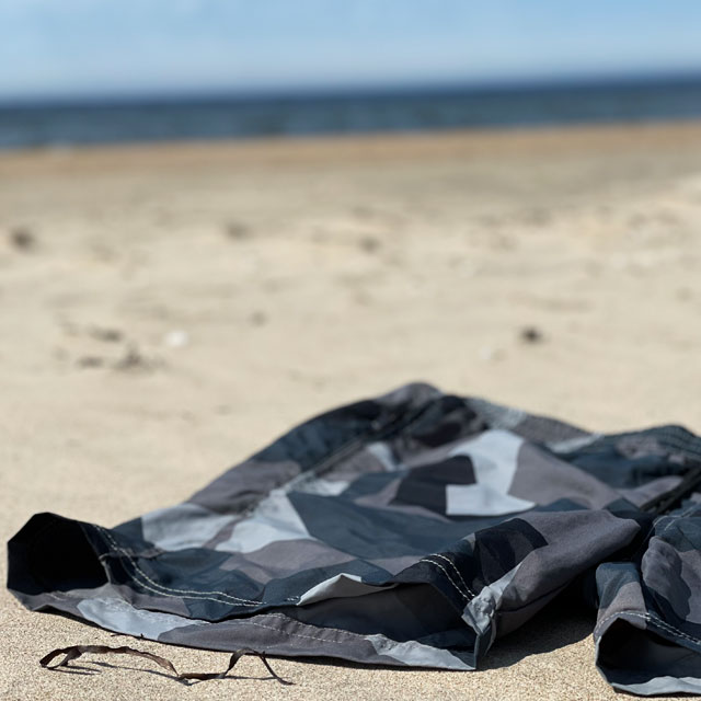 A closer look on a pair of POSEIDON Swim Shorts M90 Grey from TAC-UP GEAR laying on the sand on a beach