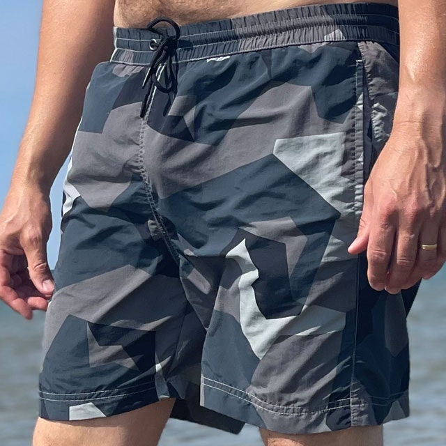 POSEIDON Swim Shorts M90 Grey seen from the front at a slight angle on model with ocean as background