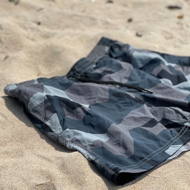 Closeup on a pair of POSEIDON Swim Shorts M90 Grey lying flat on the beach