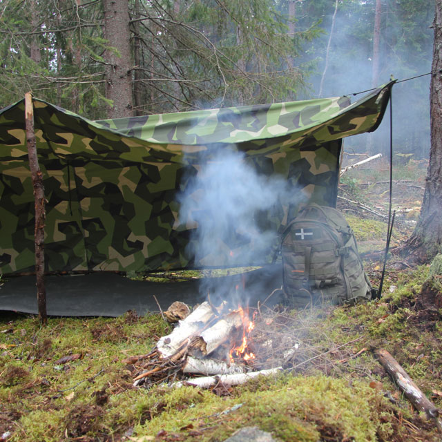 L-shape configuration of the Tarp Poncho M90 with a camp fire burning in the Swedish forest.