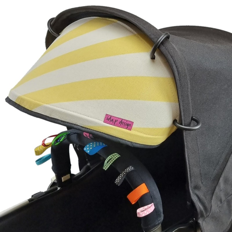 Solskydd till barnvagn sytt av ett gult och vit randigt tyg. Svart kantband och offwhite baksida.