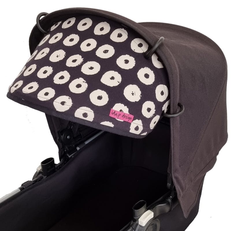 Solskydd för barnvagn. Sytt av ett handtryckt svart tyg med benvita cirklar.