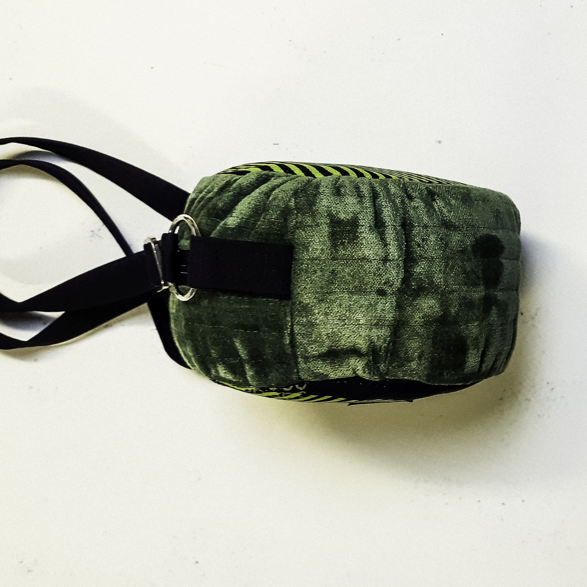 Rund väska sedd från sidan i grönt "sammetstyg" med svart bärrem