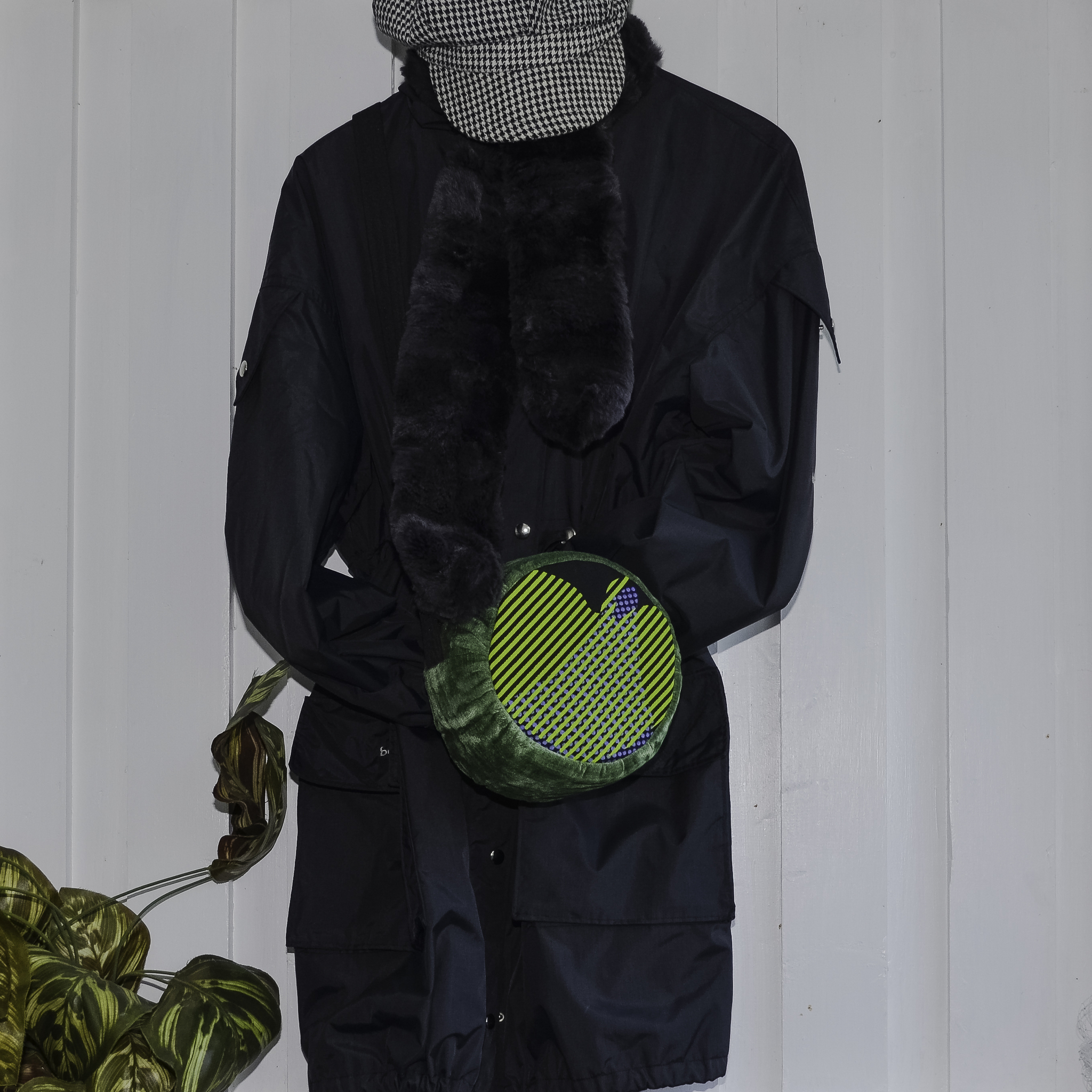 Rund väska med gröna blad i hjärtform hänger på svart kappa