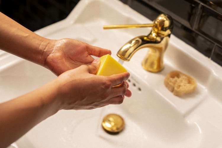 Händer som tvättar sig med fast tvål Sensitive Skin från Organics By Sara. Tvålen är tillverkad av Malin i Ratan. Bilden ger en härlig känsla vid ett vackert handfat med kopparkran.