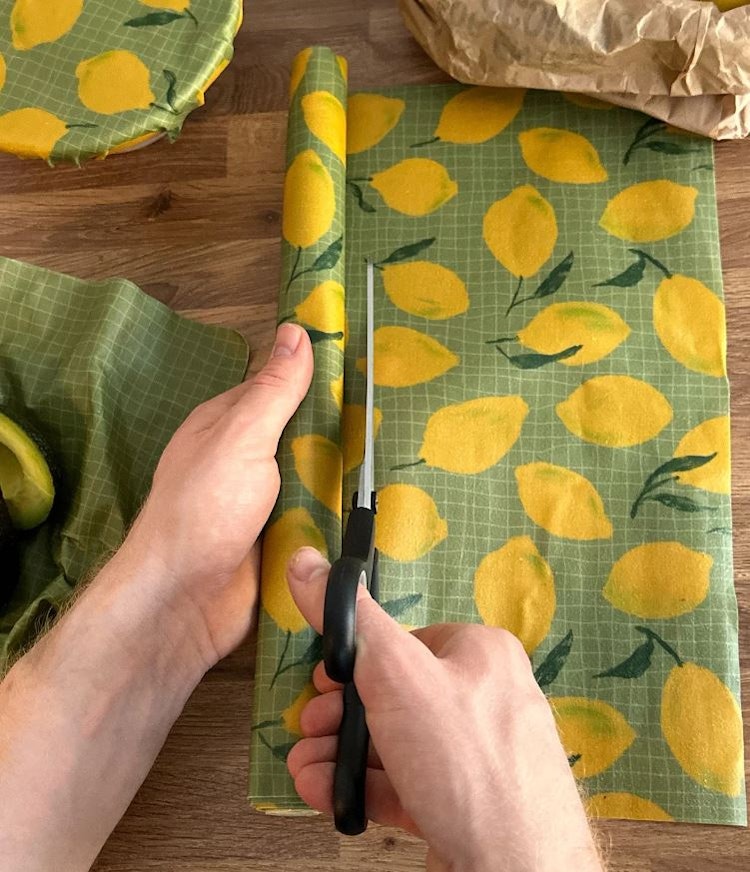 En person som klipper en bit från bivaxrullen med citronmönster