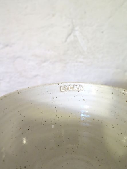 Kopp med fat i stengods, vit glasyr, text "Lycka" på insida av kopp