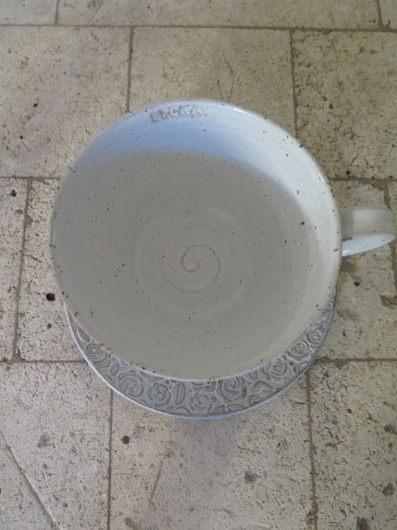 Kopp med fat i stengods, vit glasyr, text "Lycka" på insida av kopp